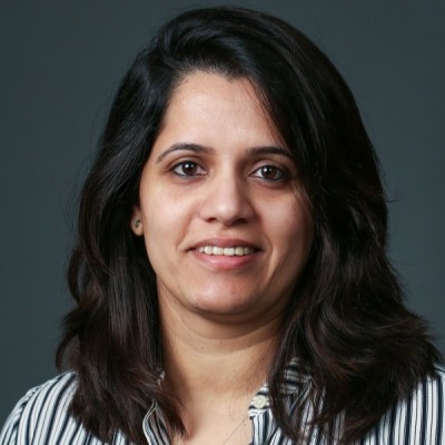 Headshot of a woman with dark shoulder-length hair, wearing a black-and-white striped blouse, smiling at the camera against a dark gray background.